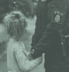 En polis håller ett barns händer i sina medan barnet tittar bort.