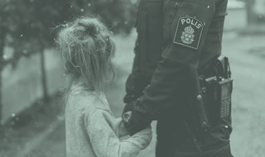 En polis håller ett barns händer i sina medan barnet tittar bort.