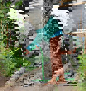 person som vattnar plantor i ett växthus i förd luvtröja och tofflor