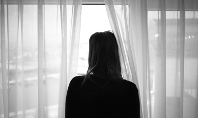 Kvinna står vänd mot fönster och blickar ut.